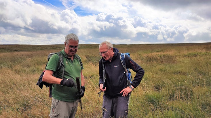 Two volunteers from the survey group at Marsden Moor stand side-by-side analysing a peat sample taking from the moor.